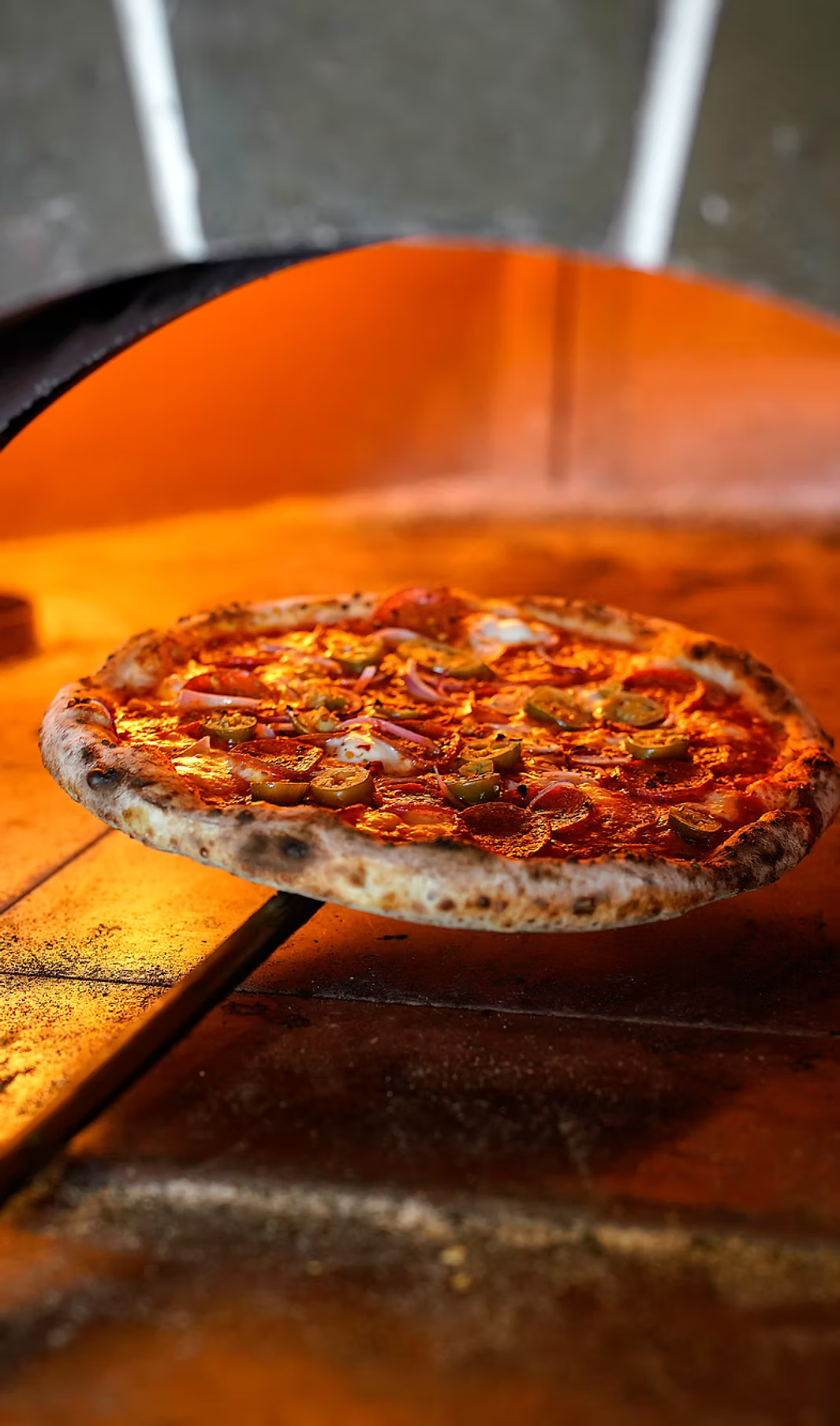 A pepperoni pizza with a beautifully charred crust inside a hot pizza oven.